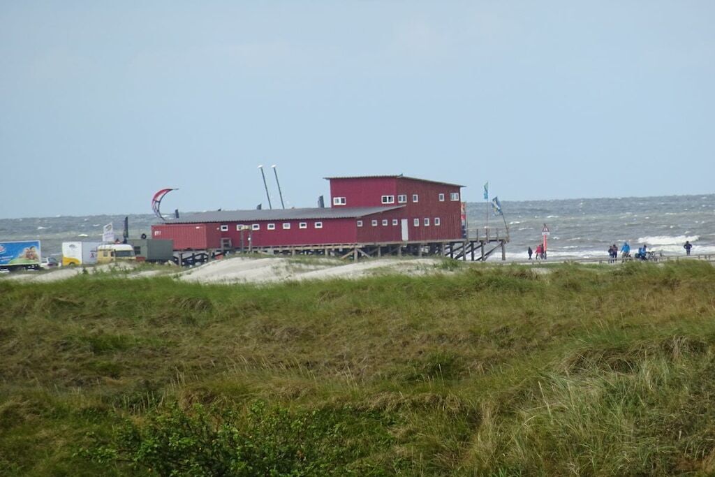 Un bâtiment rouge avec un toit plat, une petite terrasse et, au fond, une plage de sable.