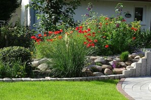 Un jardin aménagé avec une grande variété de plantes et de fleurs, un mur de soutènement en pierre et un chemin sinueux menant à une maison.