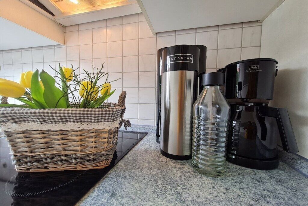 A kitchen counter with a coffee maker, a thermos, a water bottle, and a wicker basket with flowers.