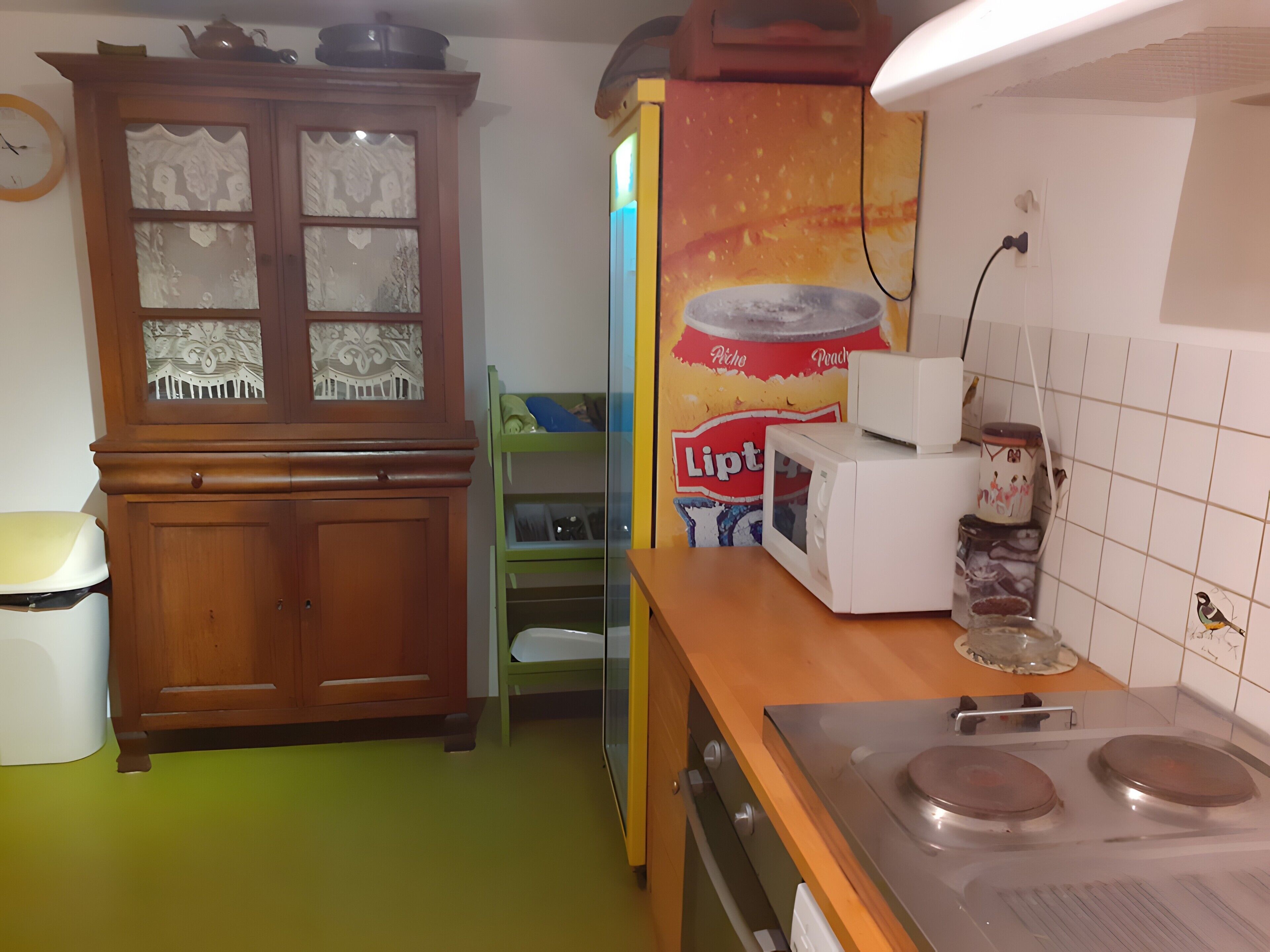 Een keuken met een houten kast, een magnetron, een fornuis en een groene stoel.