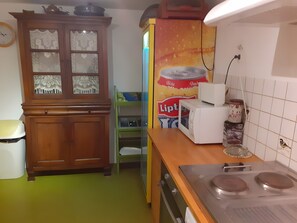 A kitchen with a wooden cabinet, a microwave, a stove, and a green chair.