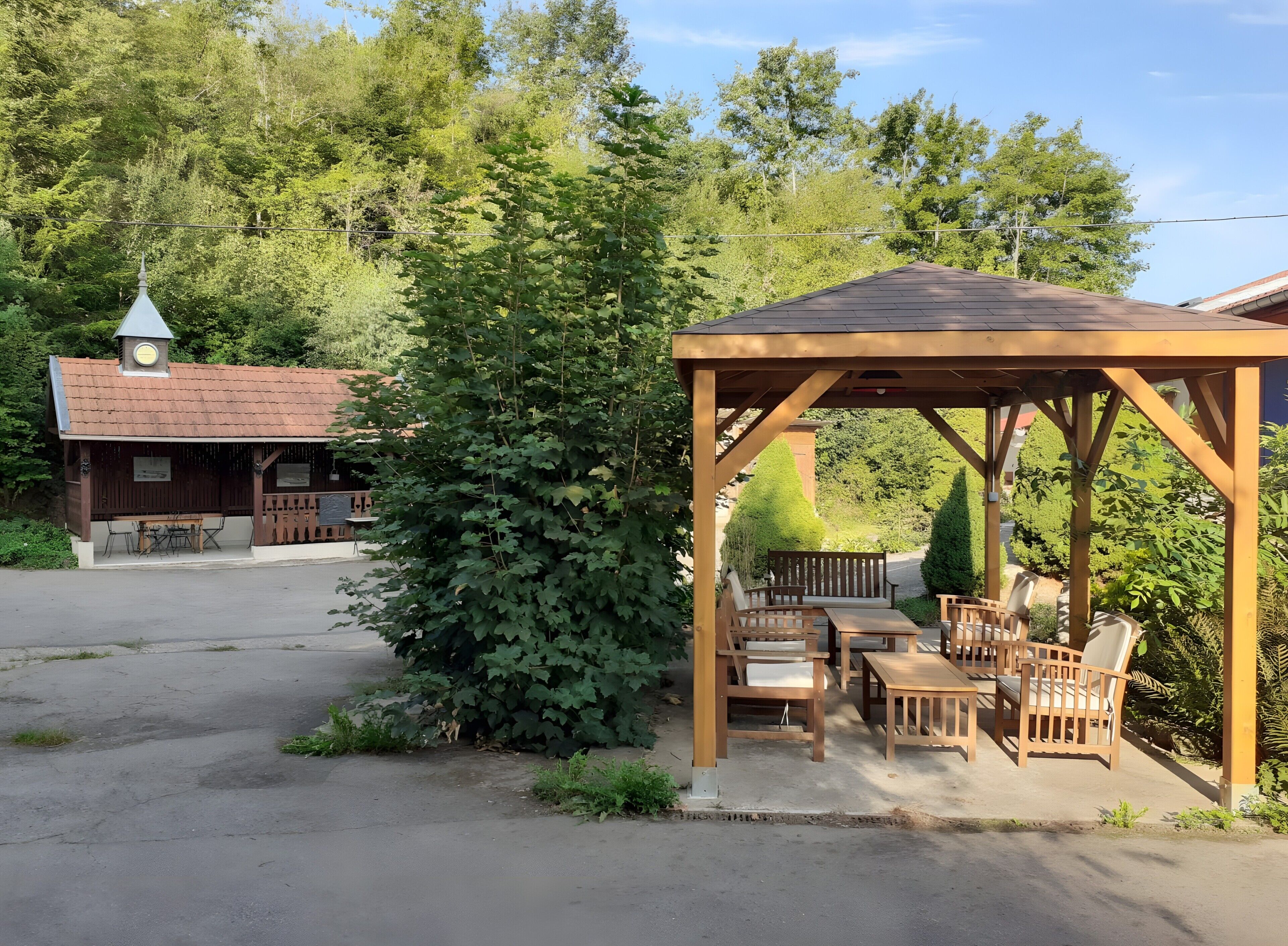 Un gazebo in legno con posti a sedere e un tavolo, immerso nel verde.