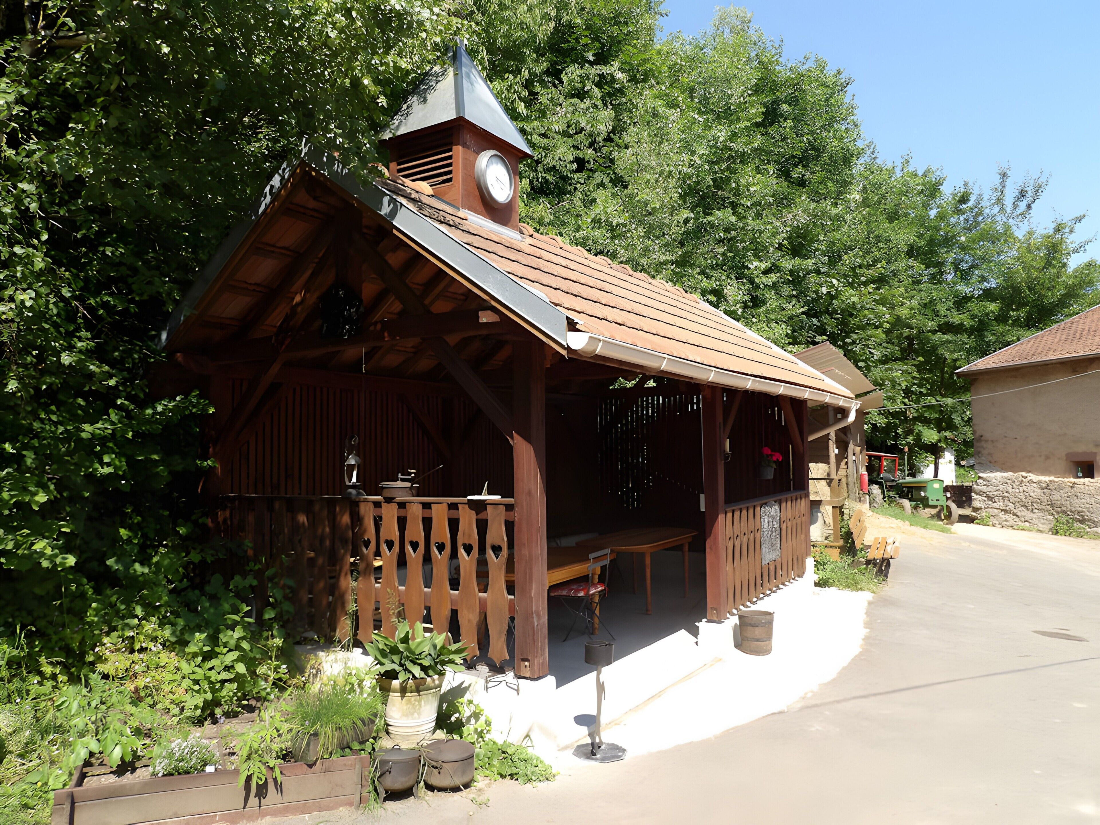 A rustic wooden building with a clock tower, surrounded by greenery and a paved driveway.
