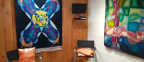 Ein Zimmer mit einem großen abstrakten Gemälde, zwei Stühlen, einem Fernseher und einer Holzwand.
