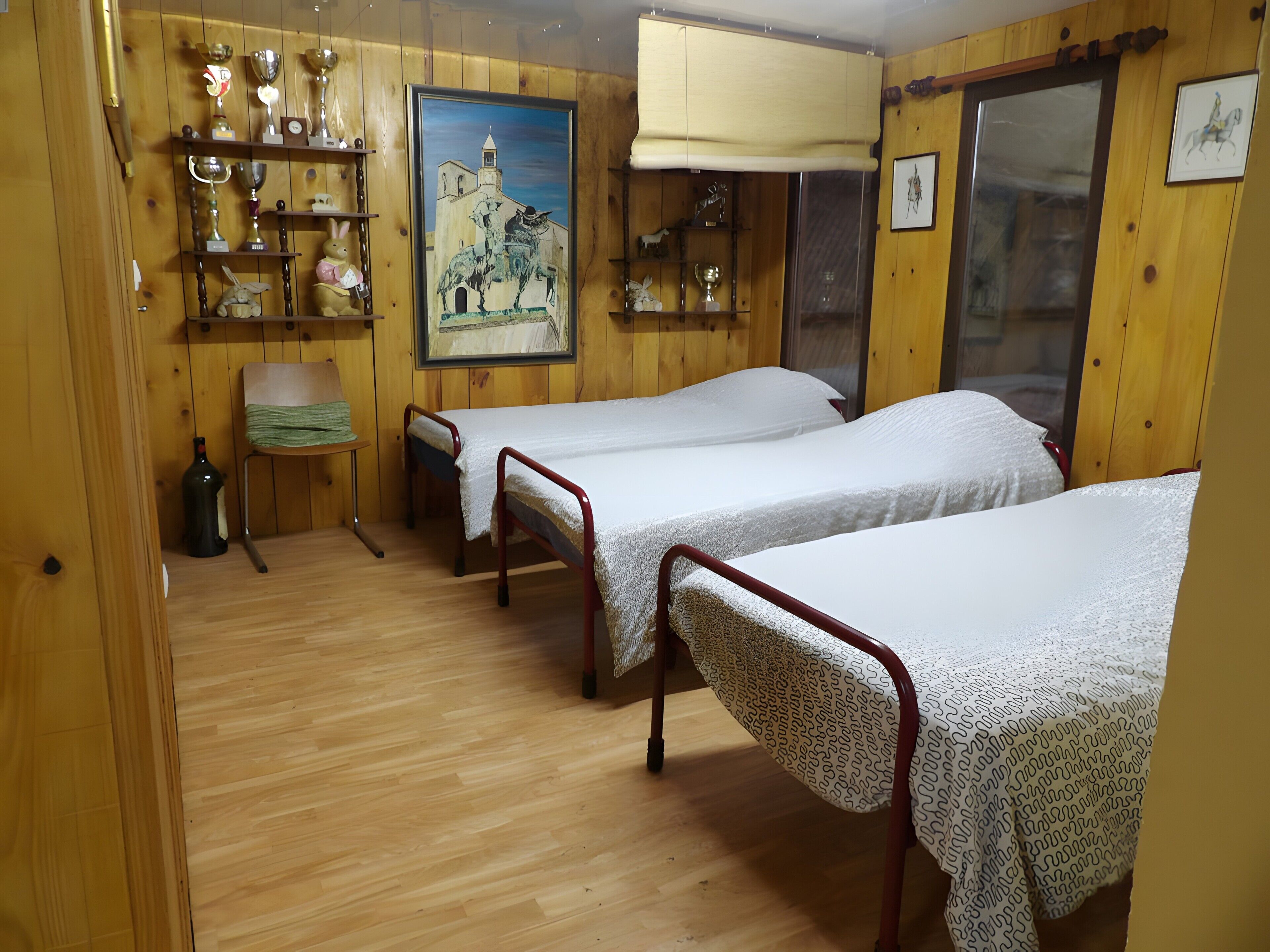 Une chambre avec deux lits simples, des murs en bois, un tableau et une étagère où sont exposés des trophées.