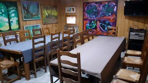A dining area with wooden tables and chairs, artwork on the walls, and a television mounted on the wall.