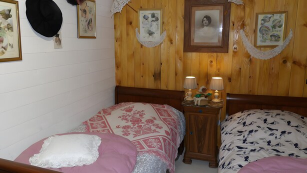 A bedroom with two single beds, wooden headboards, a nightstand with lamps, and wall-mounted decorations.