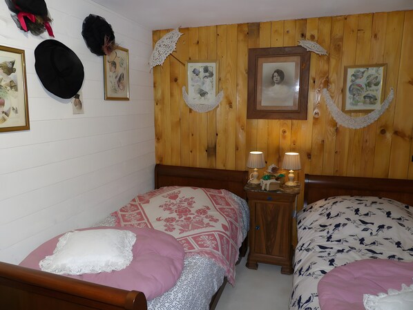 A bedroom with two single beds, wooden headboards, a nightstand with lamps, and wall-mounted decorations.