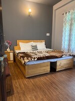 A bedroom with a wooden bed, a nightstand, a wall-mounted light, and a window with curtains.