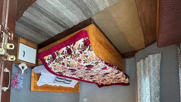 A room with a ceiling fan, a bed with a floral bedspread, a wall with a floral mural, and a framed picture.
