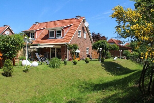 Een huis met twee verdiepingen, voorzien van een dak met rode tegels, een veranda en een verzorgd gazon.