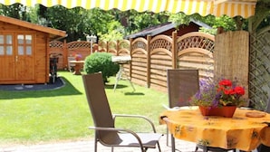 An outdoor patio with a table covered by a yellow tablecloth, a chair, and a potted plant with red flowers. - Holiday home in Aurich with swimming pool (Aurich)