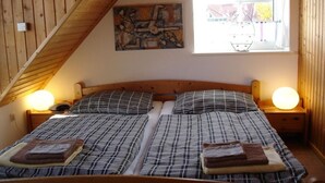 A bedroom with a wooden ceiling, a bed with plaid bedding, two bedside lamps, and a window with a view of the outside. - Holiday home in Aurich with swimming pool (Aurich)