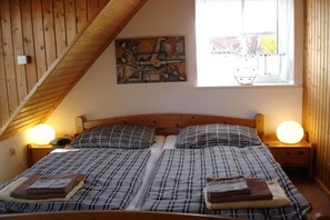 Een slaapkamer met een houten plafond, een bed met ruitdessin beddengoed, twee bedlampen en een raam met uitzicht op het buiten.