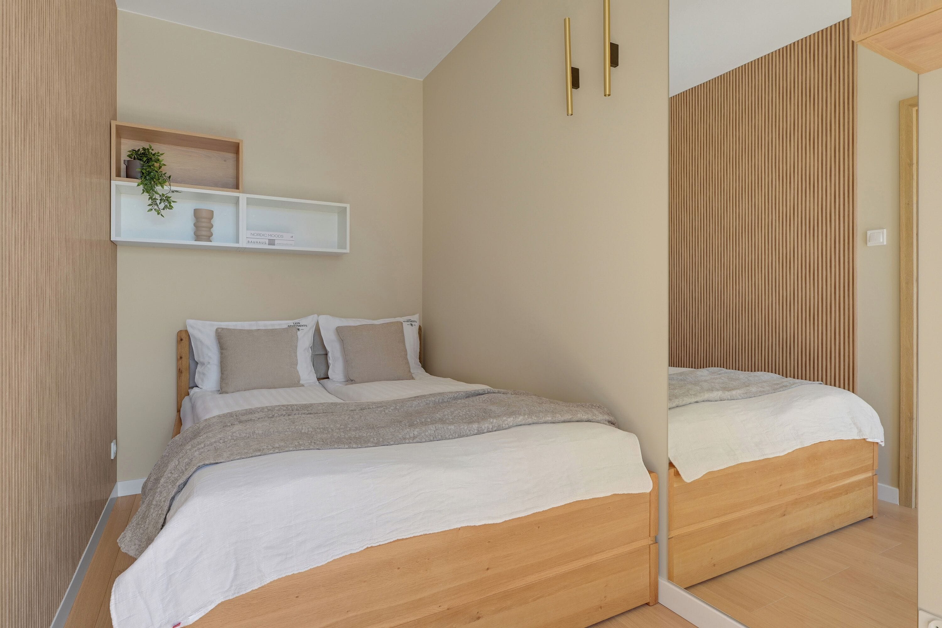 A bedroom with a bed, bedside tables, a mirror, and a shelf with decorative items.