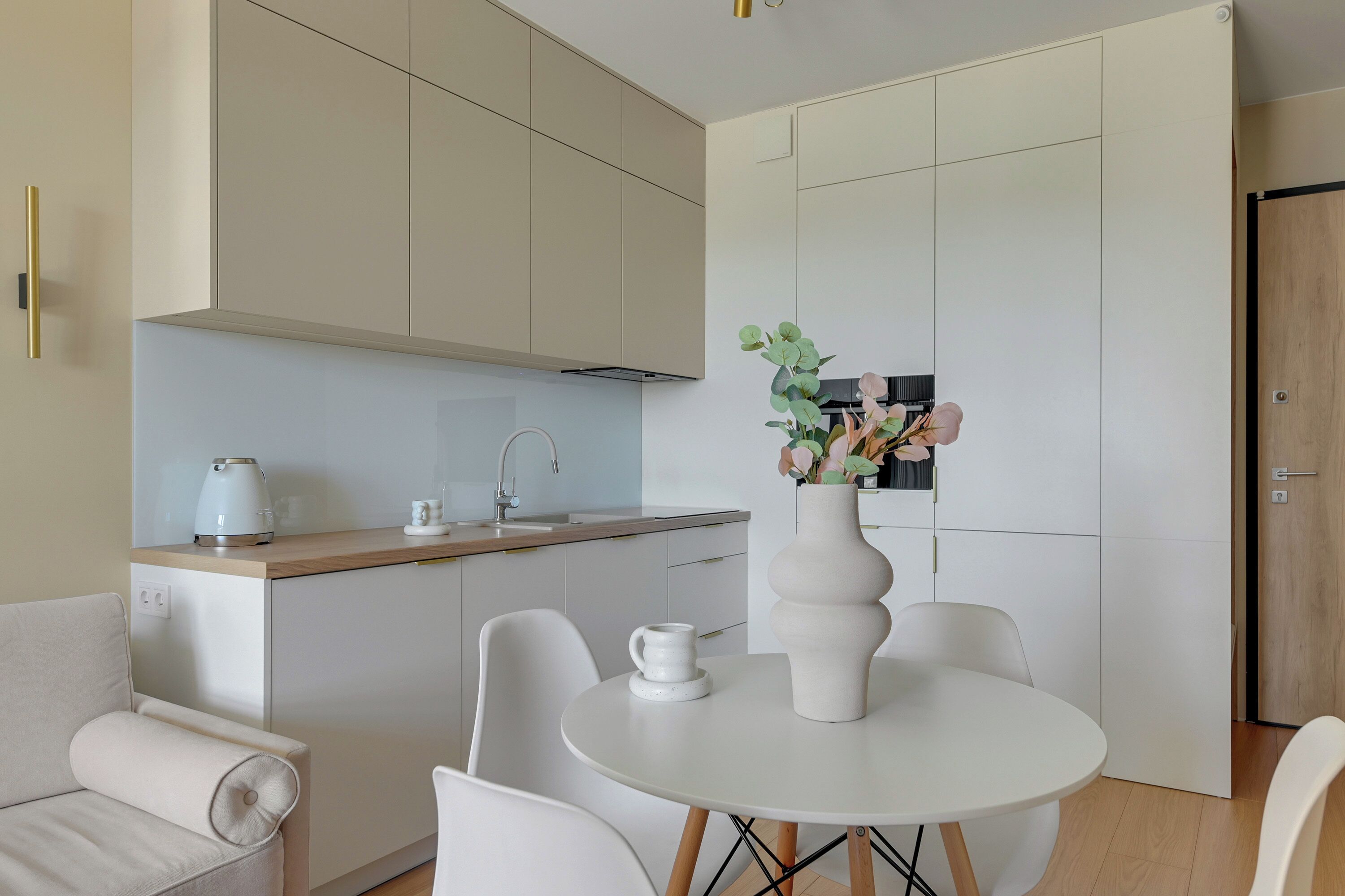 A modern kitchen with a round dining table, white chairs, and a vase with flowers.