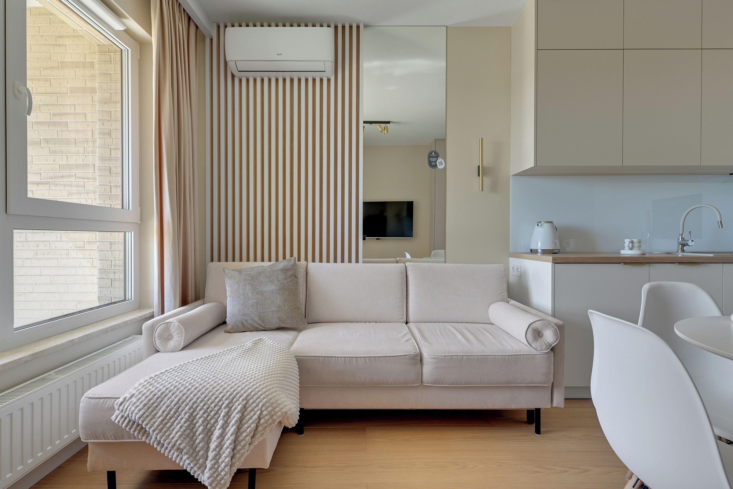 Una sala moderna con sofá, televisión y área de cocina con lavamanos y armarios.