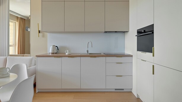 Una cocina moderna con armarios blancos, encimera de madera y horno empotrado.