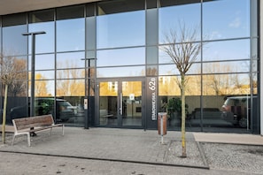 A modern building with large glass windows, a bench outside, and a tree in the foreground. - Nowa Letnica - Gdansk Seaside (Gdańsk)