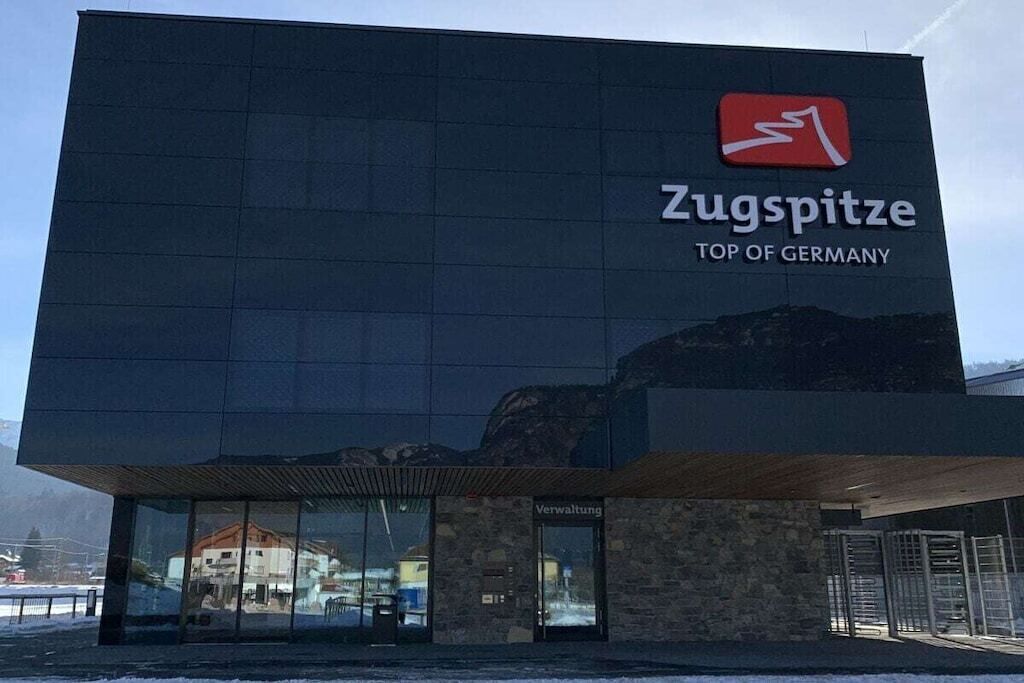 Um edifício moderno com uma fachada de vidro extensa e uma placa com a inscrição 'Zugspitze TOP OF GERMANY'.