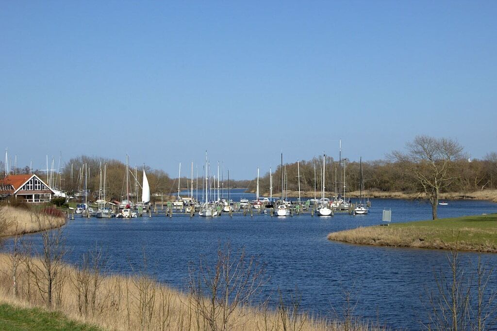 A marina with multiple boats docked, a house with a red roof, and a clear blue sky.