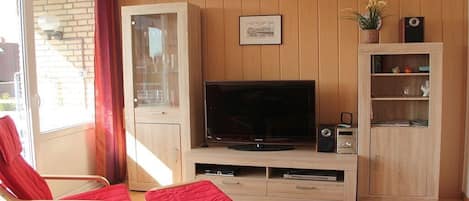 A living room with a television, wooden cabinets, and a red chair.