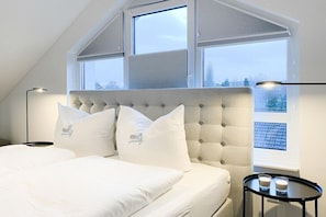 A bedroom with a large bed, a tufted headboard, and a view through the window. - Penthouse Passatstieg (Scharbeutz)