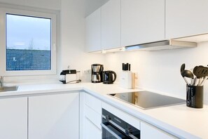 A modern kitchen with white cabinetry, a built-in oven, a coffee maker, and a knife block. - Penthouse Passatstieg (Scharbeutz)