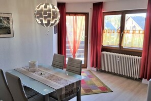 A dining area with a table, chairs, a globe light fixture, and a view of the outside through a window with curtains. - Holiday apartment in Titisee with Wi-Fi (Titisee)
