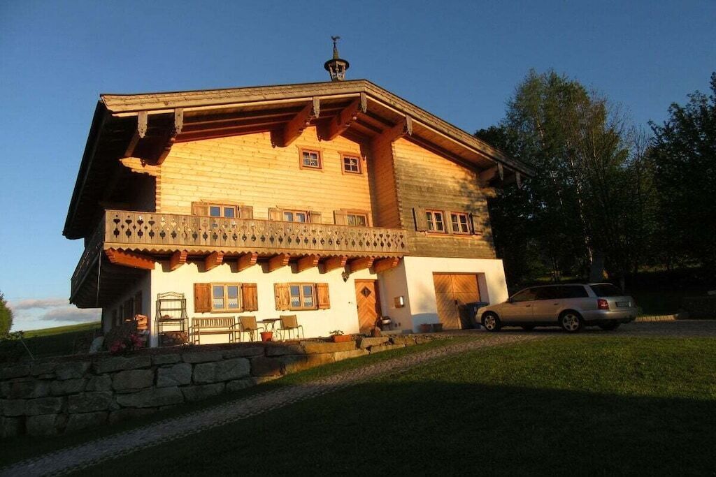 Eine Holzchalet mit Balkon, Steinmauer und einem davor stehenden Auto.