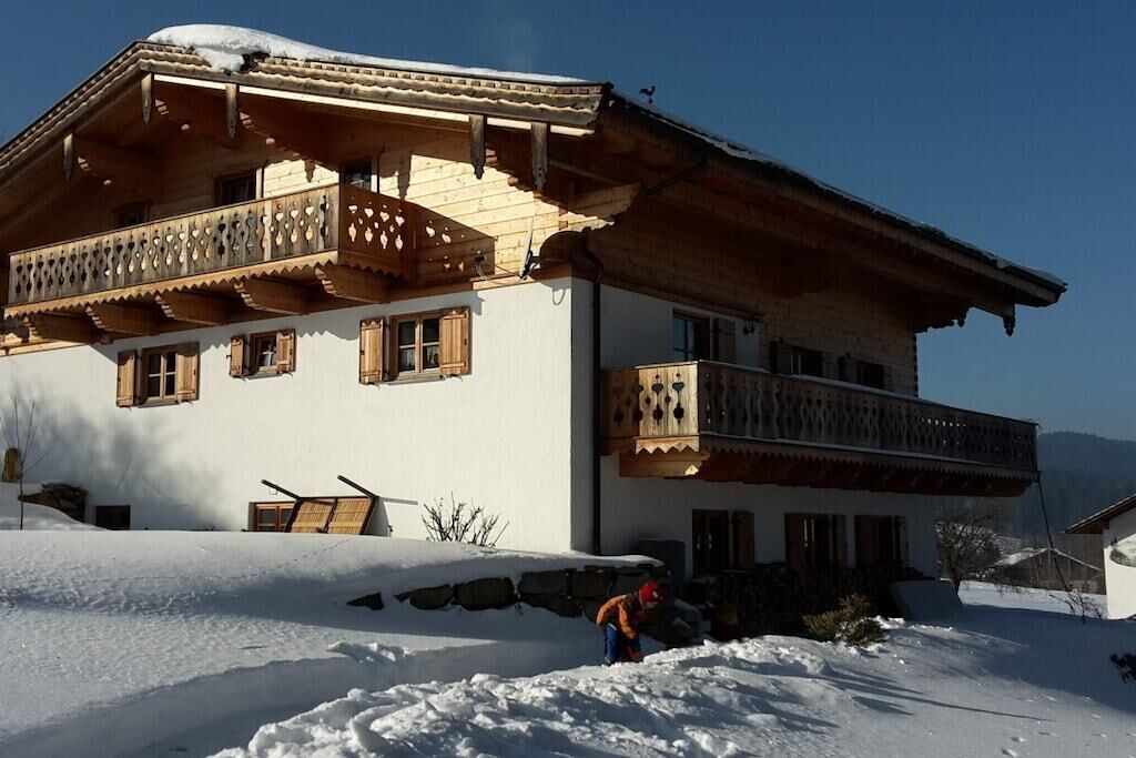 A two-story chalet with wooden balconies and a snow-covered roof.