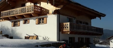 A two-story chalet with wooden balconies and a snow-covered roof.
