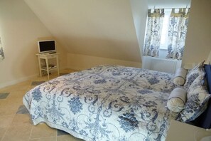 A bedroom with a bed, a TV on a stand, a window with curtains, and a radiator. - Holiday home with 1 bedroom (Katharinenheerd)