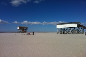 Ein Strand mit zwei Holzhütten, eine beschriftet mit 'Toilet' und die andere mit 'Toiletbox', unter blauem Himmel.