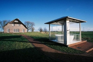 Eine moderne, gläserne Struktur mit Toilette und Dusche neben einem traditionellen Backsteinhaus.