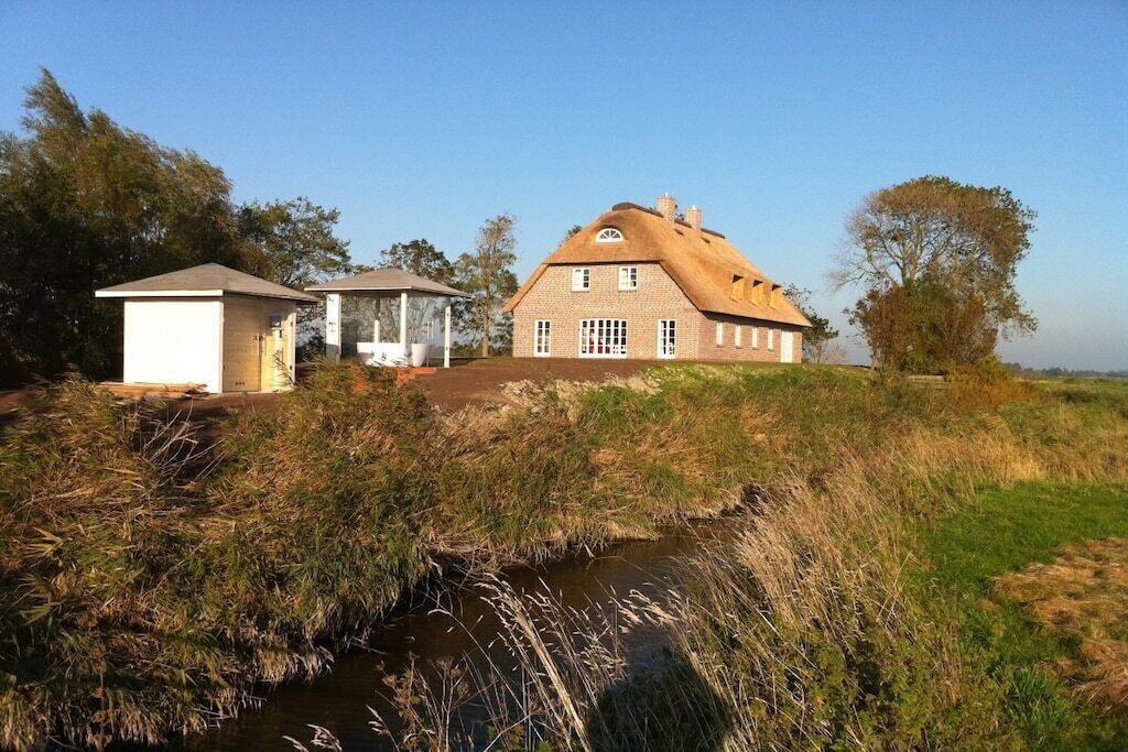 A traditional house with a thatched roof, a small adjacent structure, and a stream in the foreground.