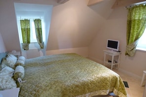 Quarto com cama, televisão sobre uma mesinha e janela com cortinas.