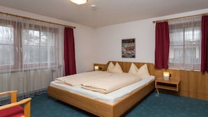 Quarto individual com uma cama e cabeceira de madeira, mesa de cabeceira com abajur e janela com cortinas leves.