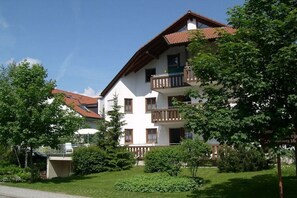 Ein mehrstöckiges Gebäude mit Balkonen, umgeben von Grünflächen und einem klaren Himmel.