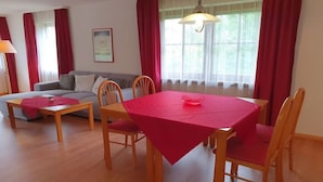 Espaço de refeições com mesa posta para quatro pessoas, sofá e luminária.
