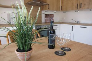 A kitchen with a potted plant, a wine bottle, and two wine glasses on a wooden table. - Holiday apartment with 2 bedrooms (Börgerende)