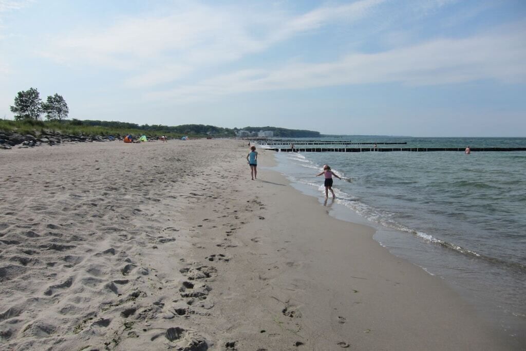 A sandy beach with footprints, a pier extending into the water, and a few tents in the background.
