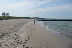 A sandy beach with footprints, a pier extending into the water, and a few tents in the background. - Holiday apartment with 2 bedrooms (Börgerende)
