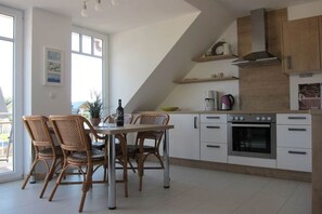 A modern kitchen with white cabinets, a built-in oven, and a dining area with wicker chairs. - Holiday apartment with 2 bedrooms (Börgerende)