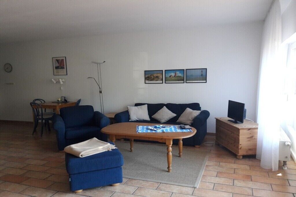 A living room with a sofa, a coffee table, a TV on a wooden cabinet, and a dining area with chairs and a table.