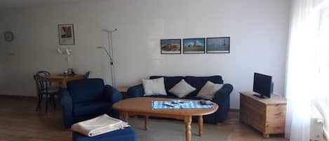 Ein Wohnzimmer mit einer Couch, einem Couchtisch, einem Fernseher auf einer Holzkommode und einem Essbereich mit Stühlen und Tisch.