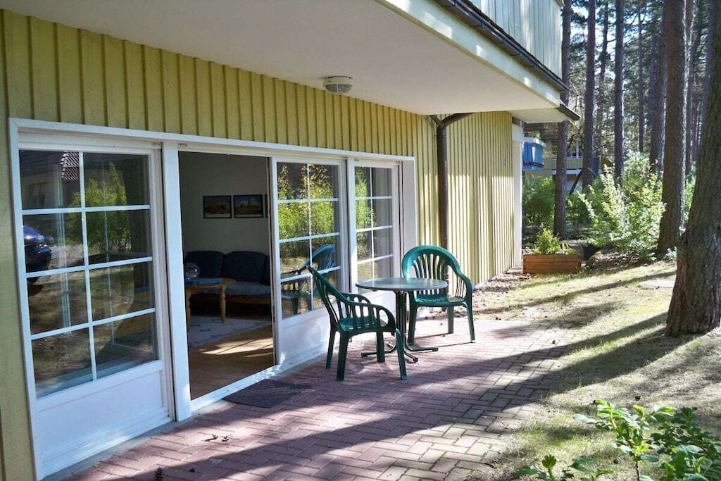 A covered patio with a brick floor, two green chairs, and a table.