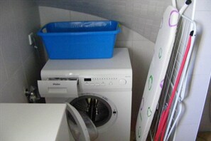 A laundry area with a white washing machine, a blue laundry basket, and a white dryer with a red cord. - Chalet Belair Schmidt (Wurster Nordseeküste Ortsteil Dorum-Neufeld)