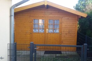 A wooden cabin with a pitched roof, a double door with windows, and a metal gate in front. - Chalet Belair Schmidt (Wurster Nordseeküste Ortsteil Dorum-Neufeld)