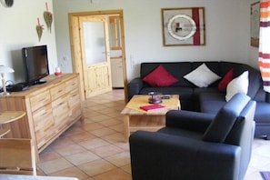 A living room with a black sofa, wooden cabinet, and a television on a wooden stand. - Chalet Belair Schmidt (Wurster Nordseeküste Ortsteil Dorum-Neufeld)